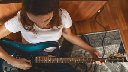 From above Young caucasian brunette woman sitting on floor and playing electric guitar at home