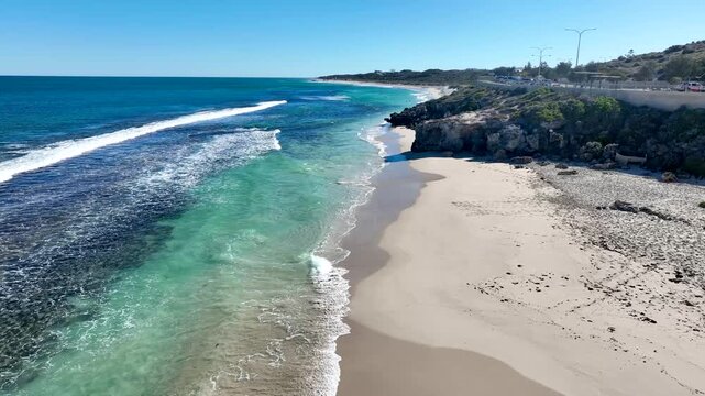 Aerial view of the pristine shoreline where turquoise waters meet a sandy beach, fringed by rocky cliffs and lush vegetation, Lancelin, Western Australia, Australia.