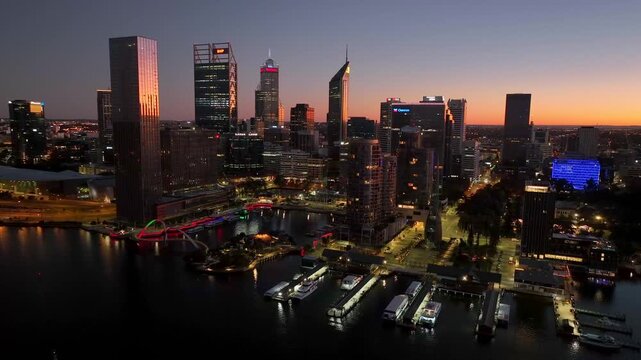 Aerial view of Perth's Central Business District skyline with illuminated skyscrapers and calm waterfront at dusk, Perth, Western Australia, Australia.