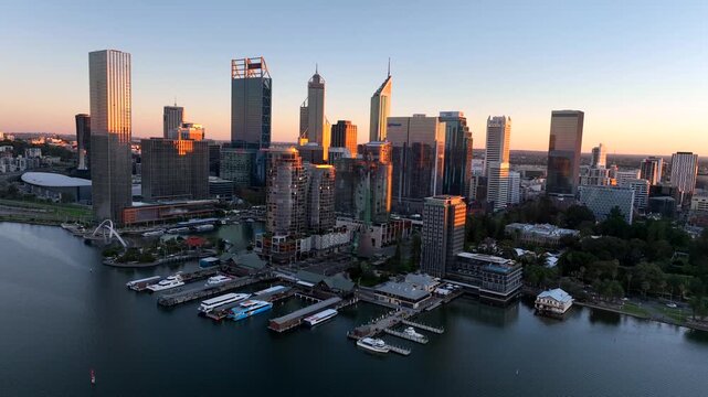 Aerial view of Perth's skyline with modern buildings reflecting sunlight, alongside docks filled with boats on the river, Perth, Western Australia, Australia.