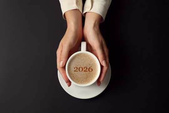 Hello New 2026 Year. Woman holding cup of coffee with numbers on black table, top view - Powered by Adobe