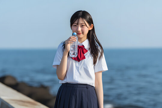 Refreshing summer portrait of a Japanese high school girl drinking water by the sea
