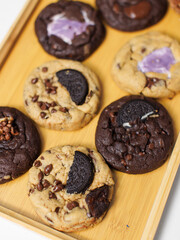 Close up freshly baked homemade chocolate soft cookies mixed toppings biscuits wafer chocolate chips on wooden board, decorate with small christmas tree, pine cones, Merry christmas and Happy new year