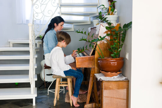 A mother teaches her son to play the piano in their home. A serene and educational moment.