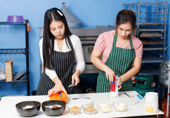 Two asian beautiful woman bakers wearing striped aprons preparing pour weigh flour in bakery kitchen measuring ingredients making homemade bread pastry teamwork baking process small business concept.