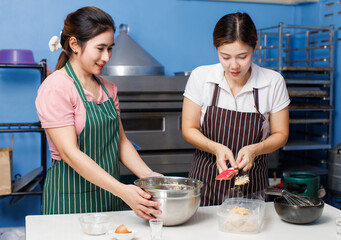 Two asian beautiful woman bakers wearing striped aprons help preparing adds butter to bowl pour flour in bakery kitchen ingredients making dough homemade bread pastry teamwork baking process concept.
