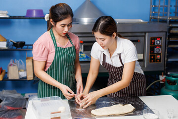 Two asian woman baker wearing striped apron preparing round fresh dough balls on metal plate table for bread pastry making, Homemade bakery process showing soft dough texture, step baking in kitchen.