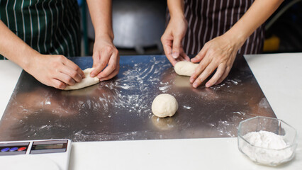 Close up hands of asian woman baker preparing round fresh dough balls on metal plate table for bread pastry making, Homemade bakery process showing soft dough texture, step baking in kitchen workspace