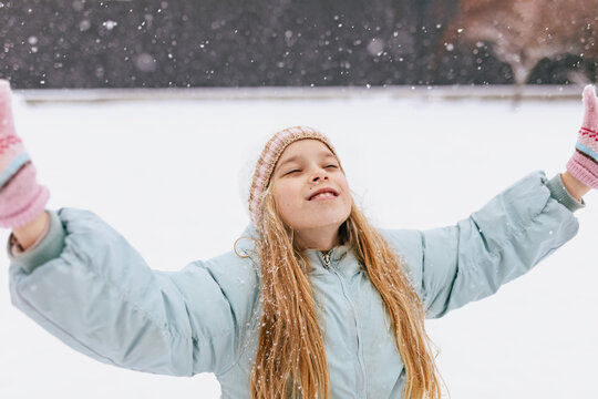 Child with blonde hair enjoying snowfall outdoors in winter wearing coat and mittens