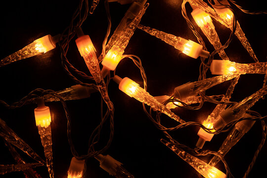 Guirlande lumineuse de No&euml;l vintage avec ampoules en forme de gla&ccedil;ons stalactites, pos&eacute;e en vrac sur fond brun fonc&eacute;, vue z&eacute;nithale, lumi&egrave;re orang&eacute;e dans la nuit