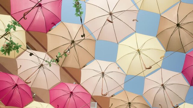Beautiful installation of colorful umbrellas hanging over a street. Pink, cream, and yellow parasols forming a canopy against a blue sky