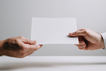 Obraz premium Two hands exchanging blank white paper sheet close up business concept neutral background document transfer agreement cooperation communication office professional