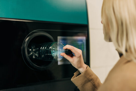 Person recycling plastic bottle at reverse vending machine indoors