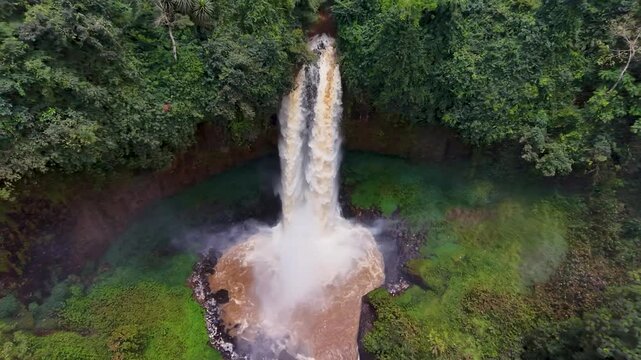 Aerial view of the powerful waterfall cascading through the lush green vegetation, contrasting with the village in the background, Bafang, West Region, Cameroon.