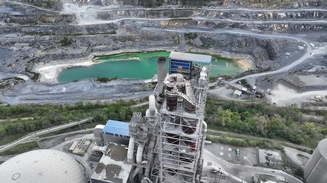 Aerial view of large industrial cement plant and open pit quarry in Martinsburg, West Virginia, USA. Factory towers, machinery and turquoise water seen from above on cloudy day. Wide shot.