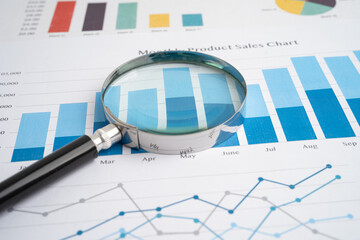 Magnifying glass on spreadsheet and graph paper.