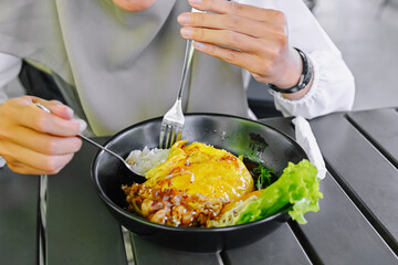 Close-up shot of hands using cutlery to enjoy a portion of Chiffon Egg Bulgogi (Omurice) at a restaurant table. Korean food and lifestyle