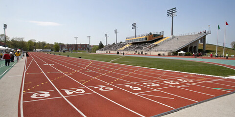 An empty outdoor running track with numbered lanes and stadium seating under a clear blue sky ready for athletic competition and training