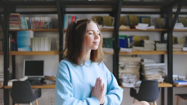 Woman practicing meditation on a table in a cozy study with books and a laptop during the afternoon