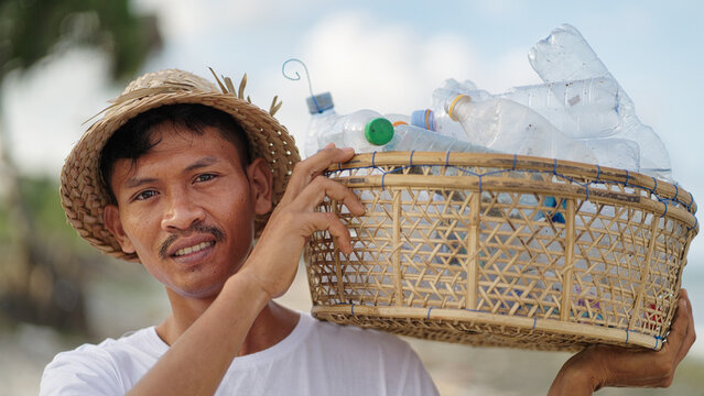 Portrait, young indonesian waster picker with plastic bottles collected for recycling, traditional hat, looking at camera serious