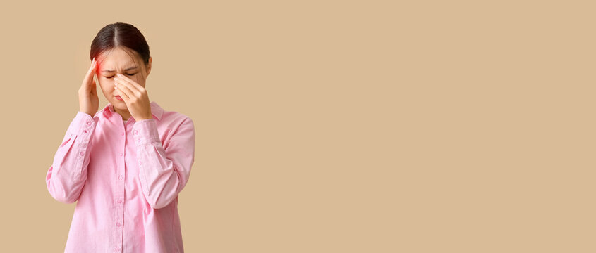 Young Asian woman suffering from headache on beige background. Brain Injury Awareness Month