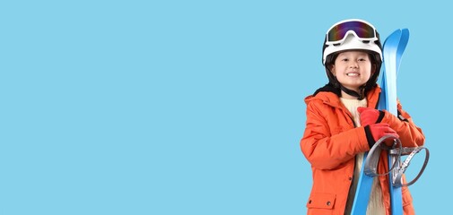 Little Asian girl with skis on blue background with space for text