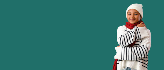 Cute African-American girl in stylish knitted hat and red scarf on green background