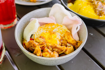 Close-up of Nasi Ayam Cangu, an Indonesian dish featuring rice topped with savory spiced chicken, fried egg, and pink prawn crackers