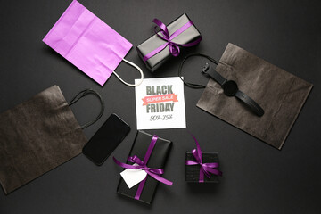 Greeting card with text BLACK FRIDAY SUPER SALE, gift boxes, shopping bags and mobile phone on dark...