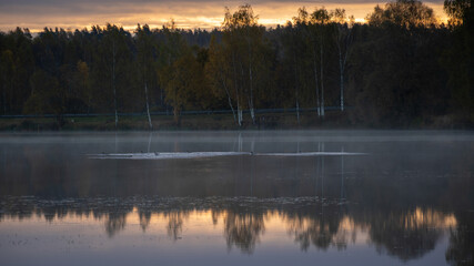 early morning by the lake, light fog over the water, trees around in autumn colors, nature in autumn