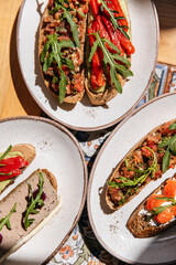 Set of appetizers bruschetta with red fish, pate, avocado, pepper and arugula in plates on the table