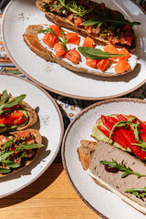 Set of appetizers bruschetta with red fish, pate, avocado, pepper and arugula in plates on the table