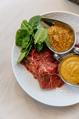 Piece of fresh red meat with mustard and spinach on a plate for barbecue steak preparation