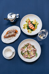 Lunch of red fish steak, prosciutto with parmesan and sweet tube with cream on a restaurant table