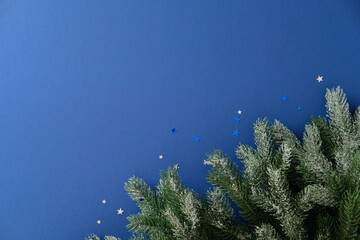 Winter holiday background with frosted evergreen branch and golden blue star confetti on blue...