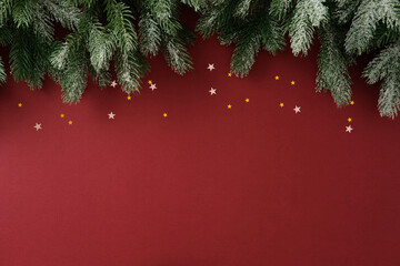 Christmas background with fir branches and star confetti on red backdrop, festive holiday template...