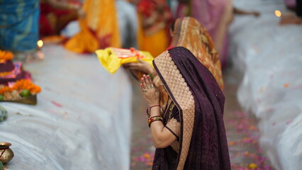Two women dressed in sarees hold offerings and pray during Chhath Puja festival, representing devotion and unity in Indian tradition.