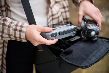 Excited individual unpacks equipment from a stylish bag, holding a drone controller and a drone, ready to capture stunning aerial views in nature.