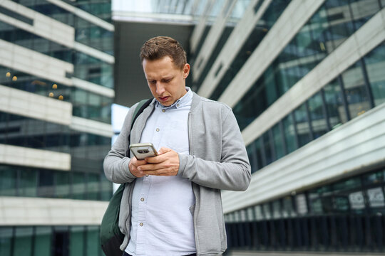 Businessman checking smartphone outside modern office - Powered by Adobe