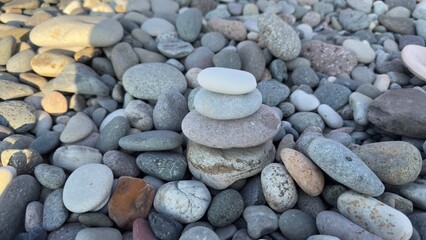 Balanced cairn of smooth rounded stones atop a pebble beach with natural assortment of various shapes, sizes, and colors under soft sunlight