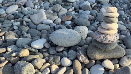 Balanced cairn of smooth rounded stones atop a pebble beach with natural assortment of various shapes, sizes, and colors under soft sunlight