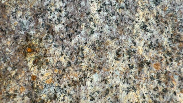Close-up of natural granite rock surface with coarse-grained texture and speckled mineral pattern in shades of gray, white, black, and orange-brown under directional light