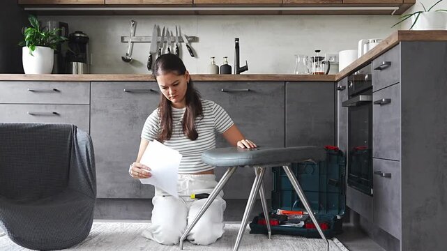 Frustrated young woman sitting on the floor reading instructions while assembling a chair. Concept of confusion and challenge in do it yourself project.