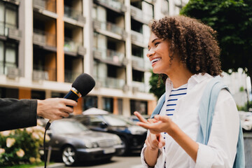 Young woman smiles during street interview in a lively urban city setting © deagreez