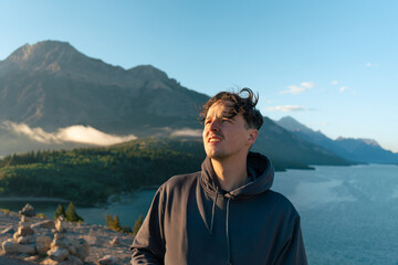 Man in hoodie gazes at scenic mountain lake landscape on a sunny day.