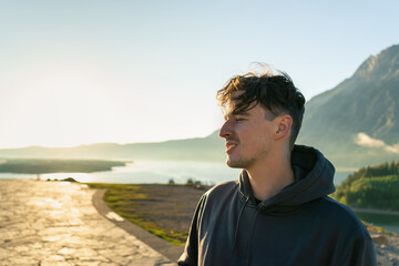 Fototapeta premium Man in a hoodie looks out at a scenic mountain and lake vista at sunrise.