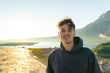 Young man in a hoodie enjoying a scenic view with mountains and a lake.