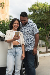 Happy couple using smartphone next to car outdoors