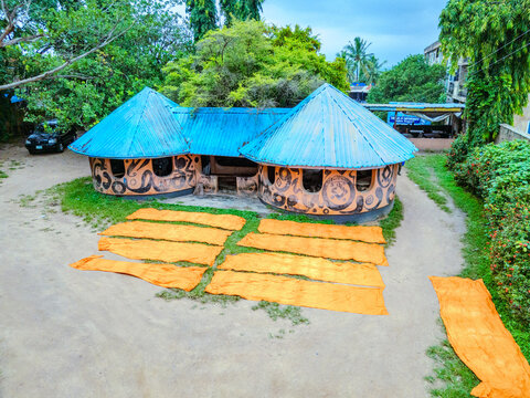 Aerial view of a round building with a bright blue roof, surrounded by green foliage, with orange fabrics laid out in the forecourt, Ede, Osun, Nigeria.