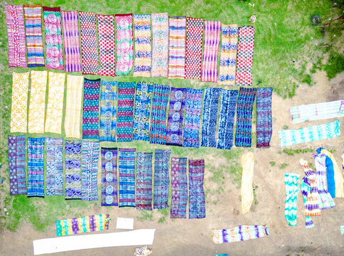Aerial view of vibrant textiles drying in the sun, their intricate patterns a colourful contrast against the green grass and earth, Ede, Osun, Nigeria.